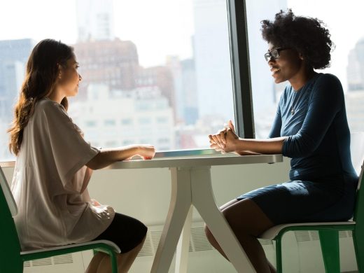 two women talking, seated at a table