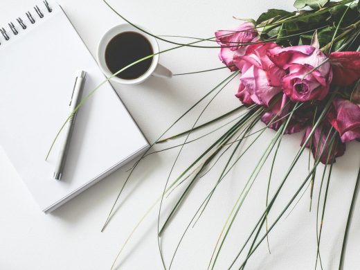 a picture of a journal beside a cup of coffee. There are also flowers on the table