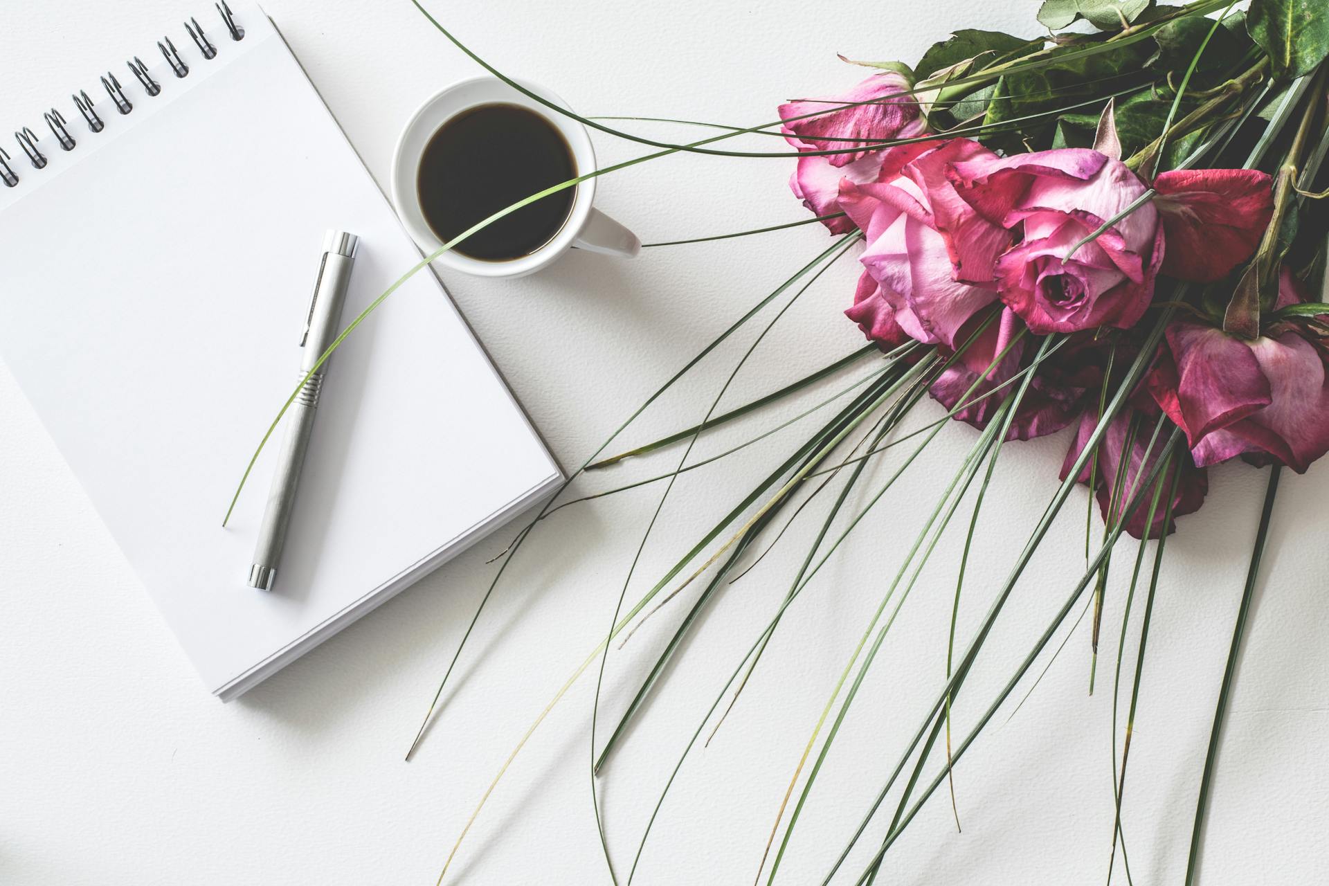 a picture of a journal beside a cup of coffee. There are also flowers on the table